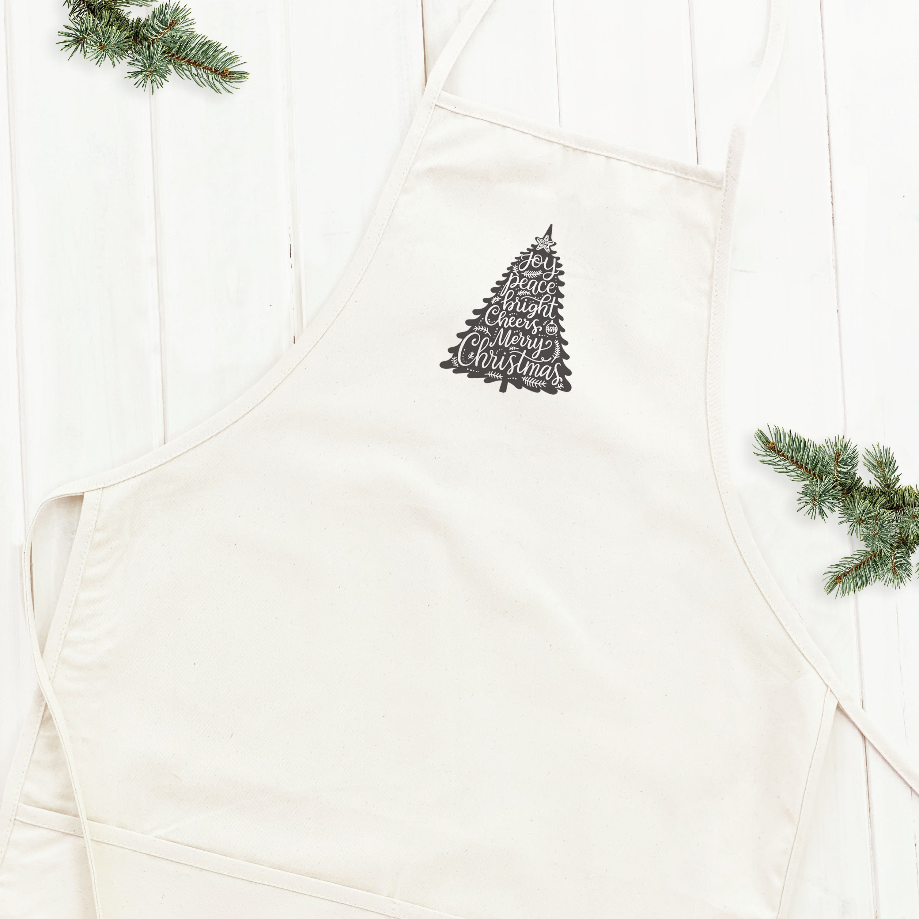 Joy Christmas Tree Women's Apron featuring festive design, adjustable neck strap, and divided front pocket, made from durable cotton canvas.