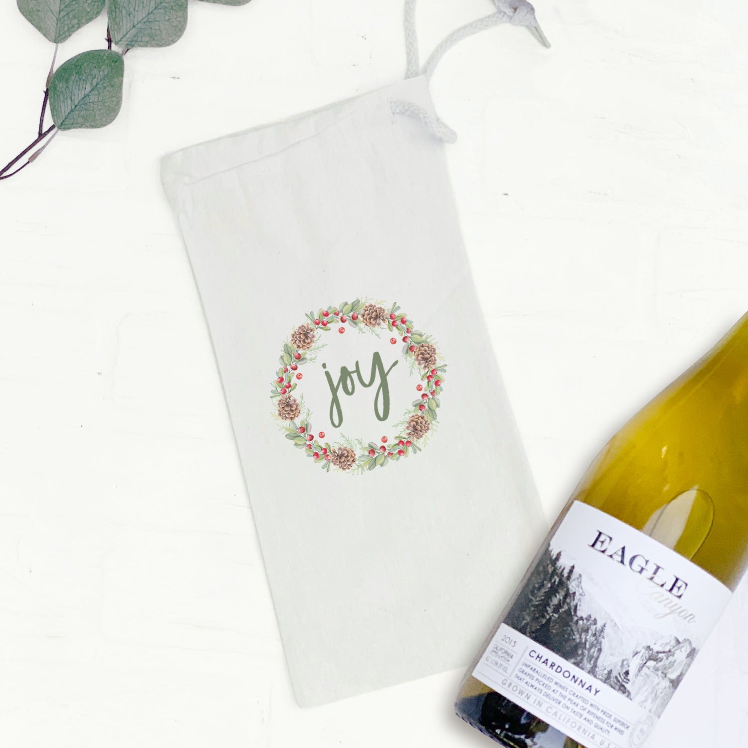 Joy Wreath Canvas Wine Bag featuring a stylish design with a matching drawstring closure, perfect for holding a standard 750mL wine bottle.