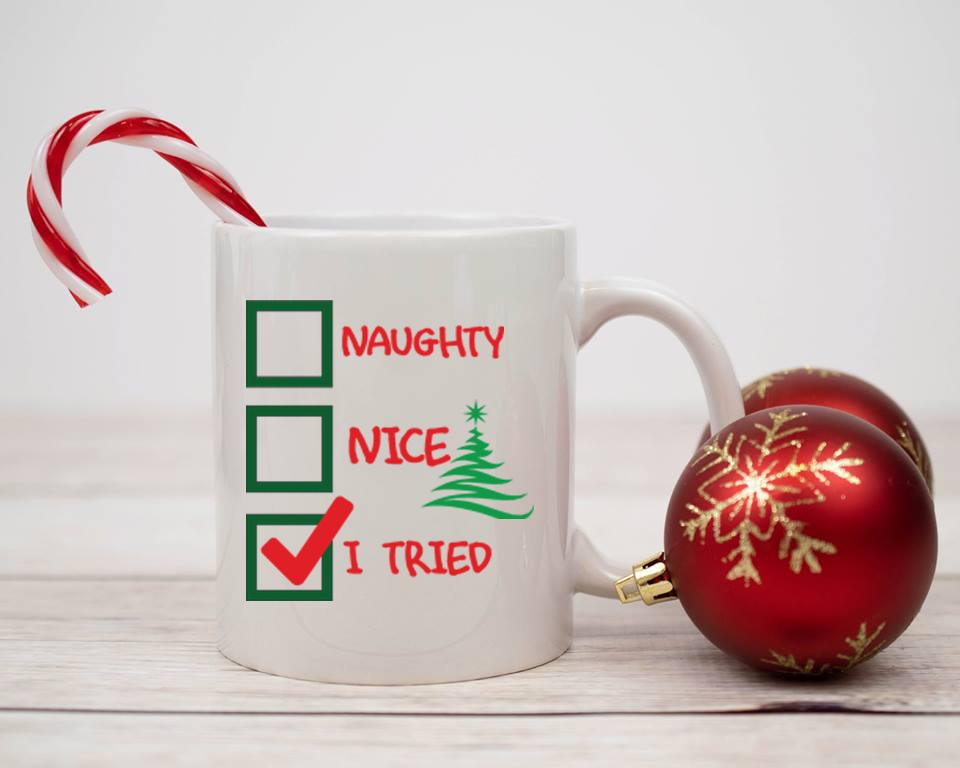 A glossy white ceramic mug with the phrase 'Naughty, Nice, I Tried' printed on it, perfect for holiday beverages.