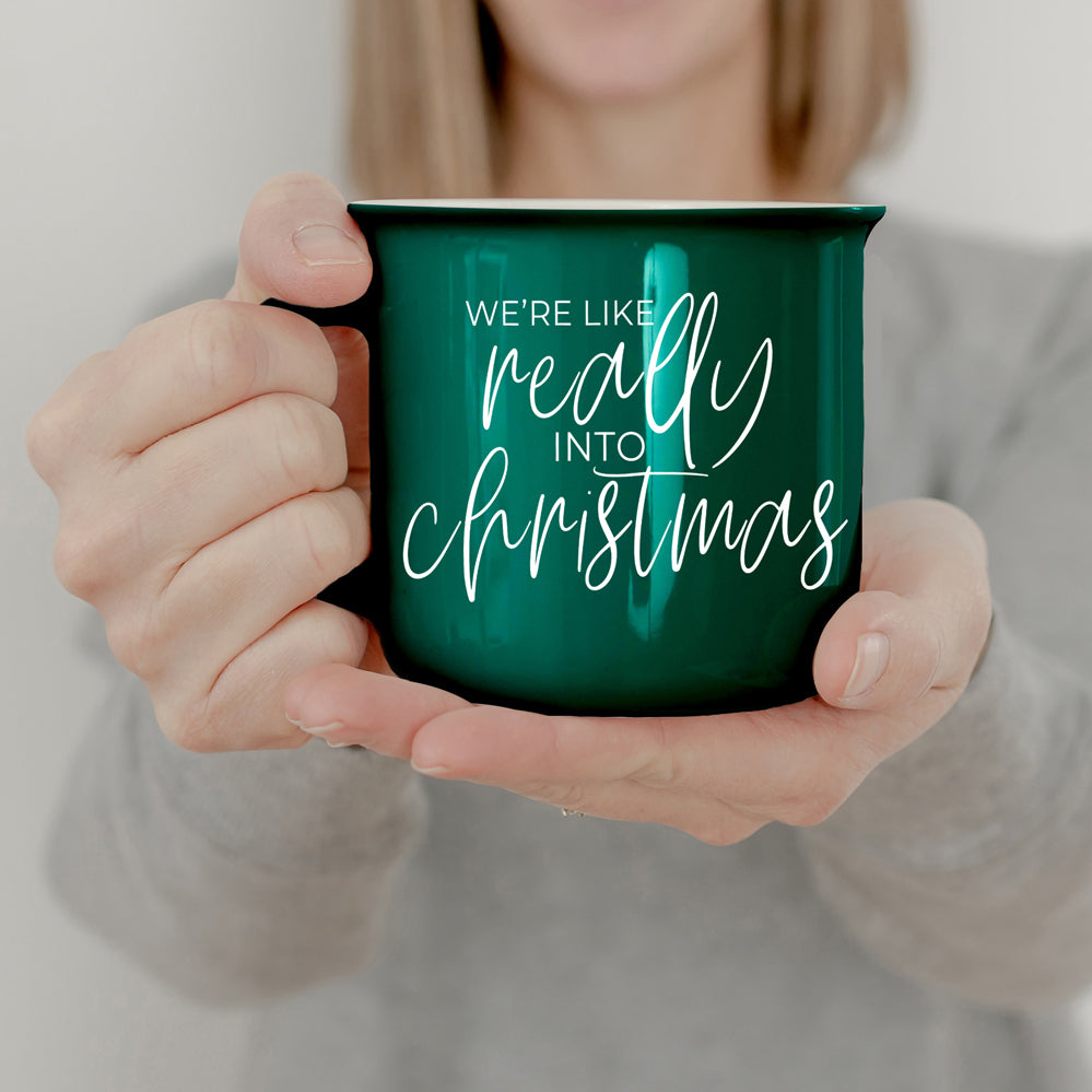 A vibrant red and green ceramic mug with white lettering, featuring a festive design on both sides, perfect for holiday drinks.