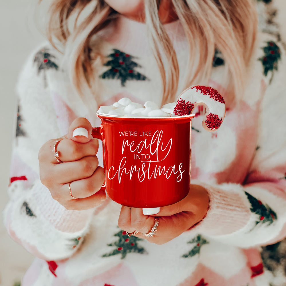 A vibrant red and green ceramic mug with white lettering, featuring a festive design on both sides, perfect for holiday drinks.