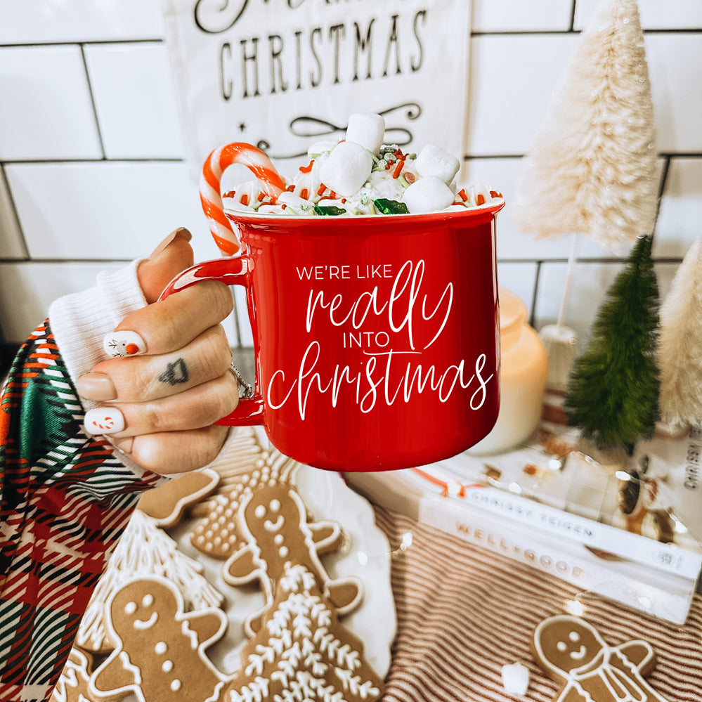 A vibrant red and green ceramic mug with white lettering, featuring a festive design on both sides, perfect for holiday drinks.