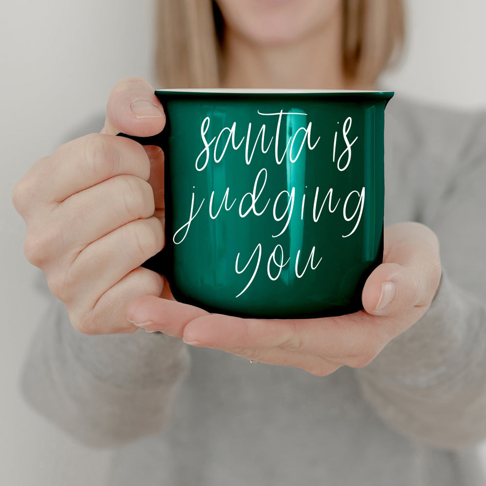 A festive ceramic mug featuring a humorous Santa design, available in red or green, perfect for holiday beverages.