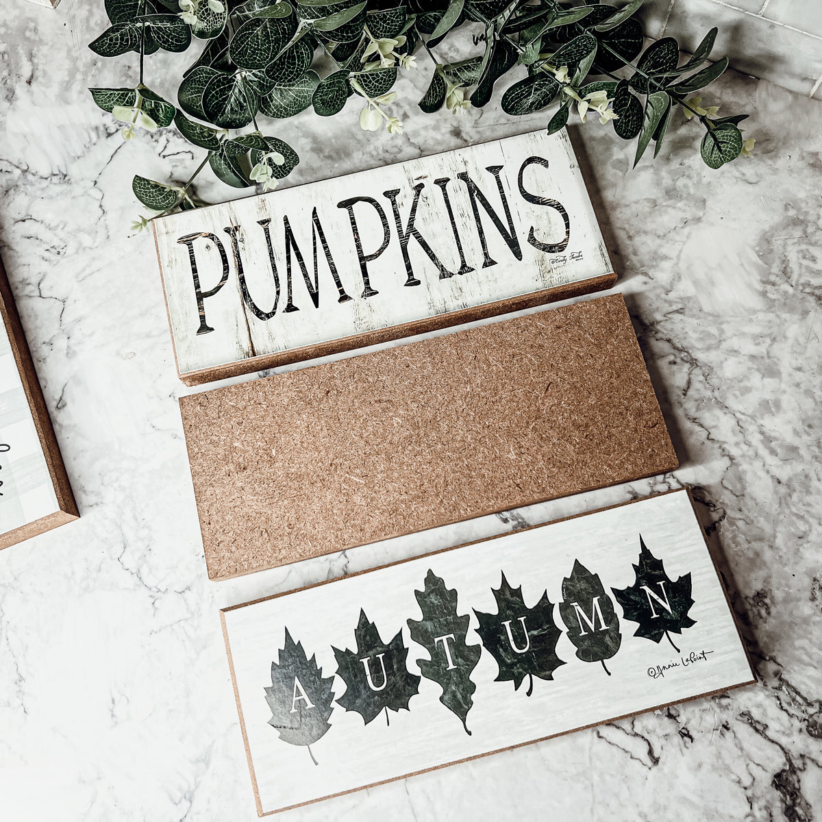 Rustic Autumn sign with off-white background and leaf designs, spelling 'Autumn' in elegant letters.