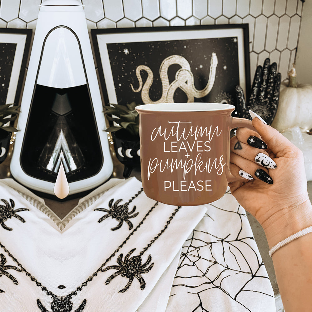 A ceramic campfire style mug featuring a neutral brown tone with white lettering that reads 'Autumn Leaves + Pumpkins Please', designed for fall.