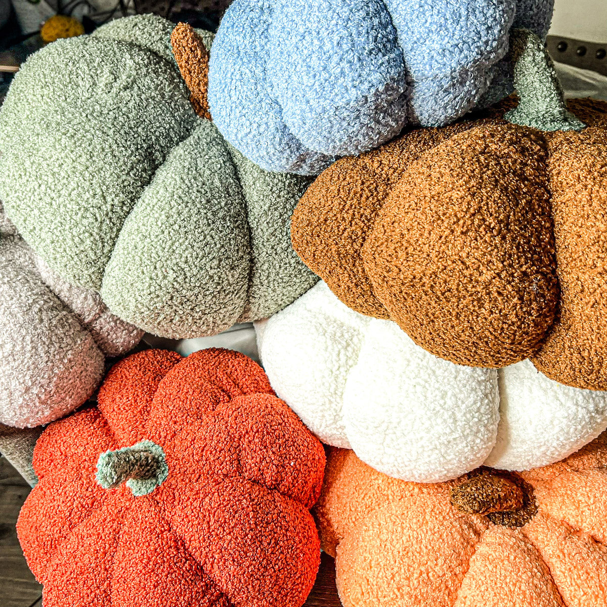 A collection of plush Blair Pumpkins in various colors including blue, gray, and orange, showcasing their soft texture and classic pumpkin shape.