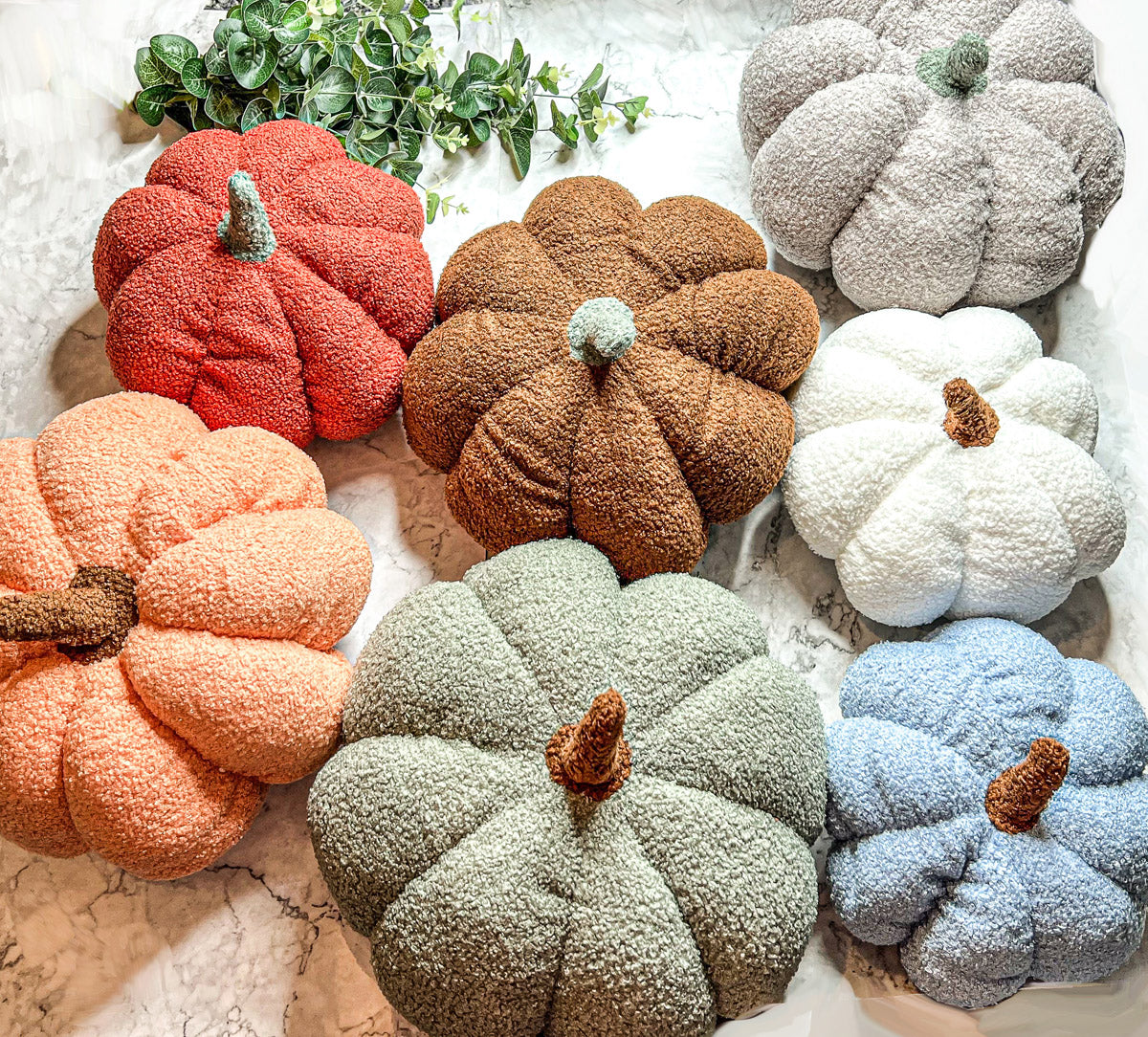 A collection of plush Blair Pumpkins in various colors including blue, gray, and orange, showcasing their soft texture and classic pumpkin shape.