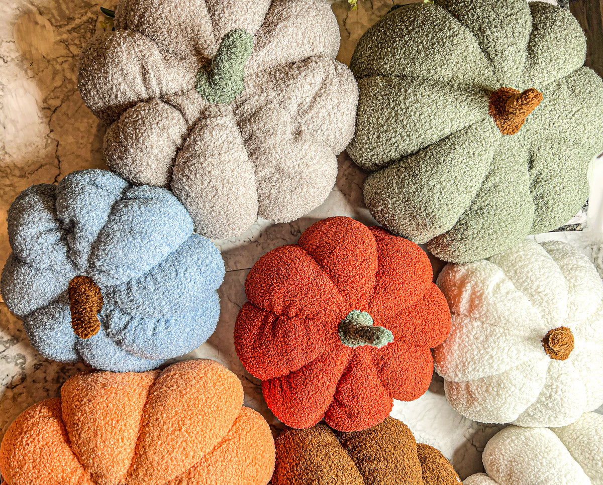 A collection of plush Blair Pumpkins in various colors including blue, gray, and orange, showcasing their soft texture and classic pumpkin shape.