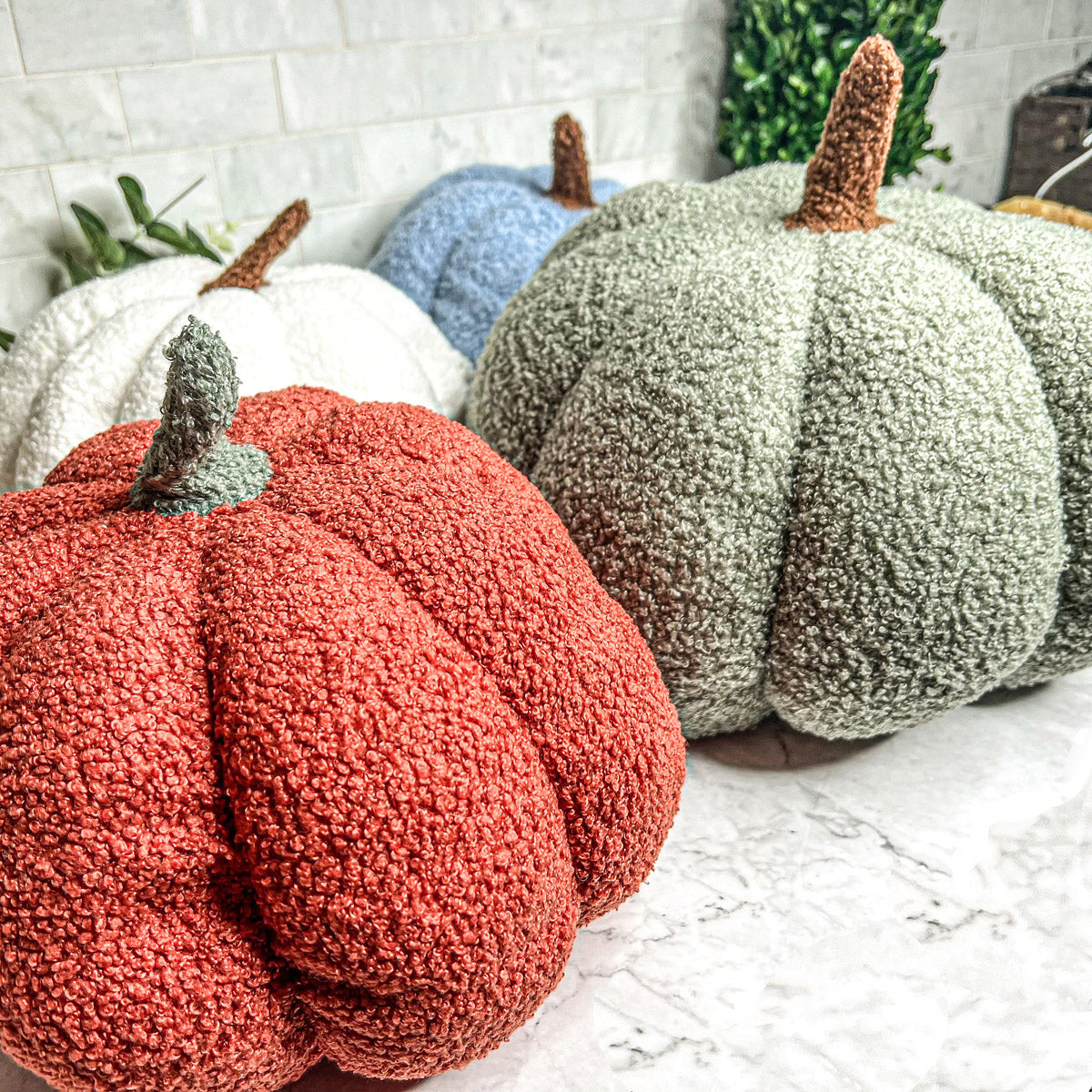 A collection of plush Blair Pumpkins in various colors including blue, gray, and orange, showcasing their soft texture and classic pumpkin shape.