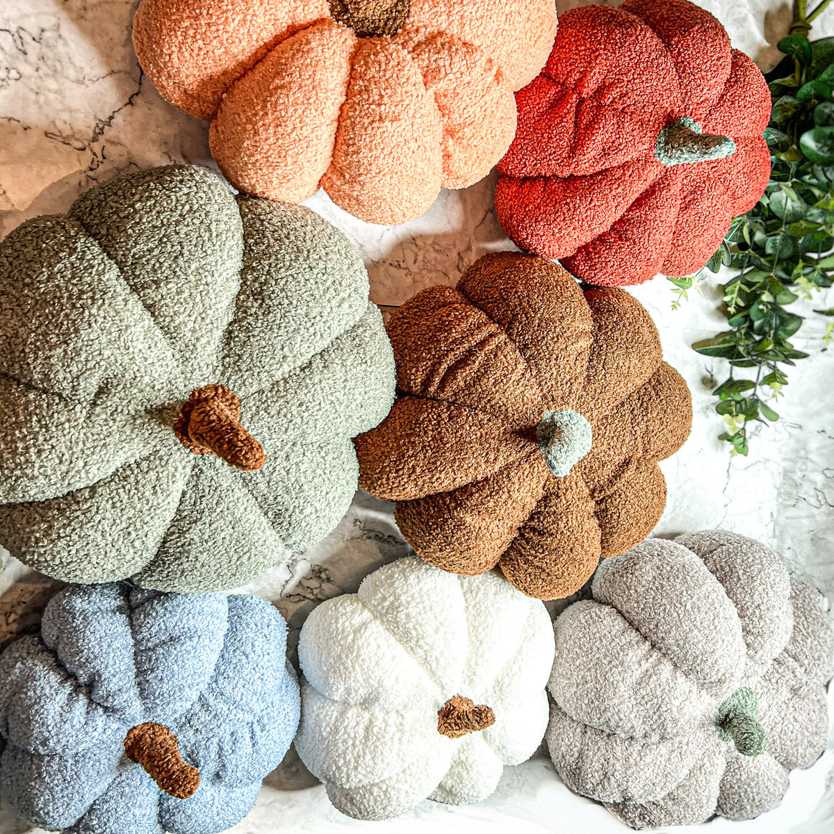 A collection of plush Blair Pumpkins in various colors including blue, gray, and orange, showcasing their soft texture and classic pumpkin shape.