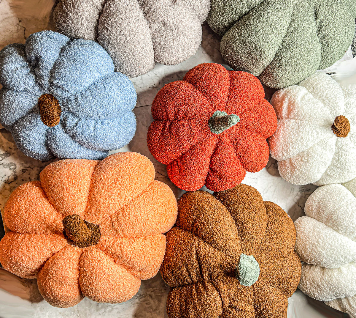 A collection of plush Blair Pumpkins in various colors including blue, gray, and orange, showcasing their soft texture and classic pumpkin shape.