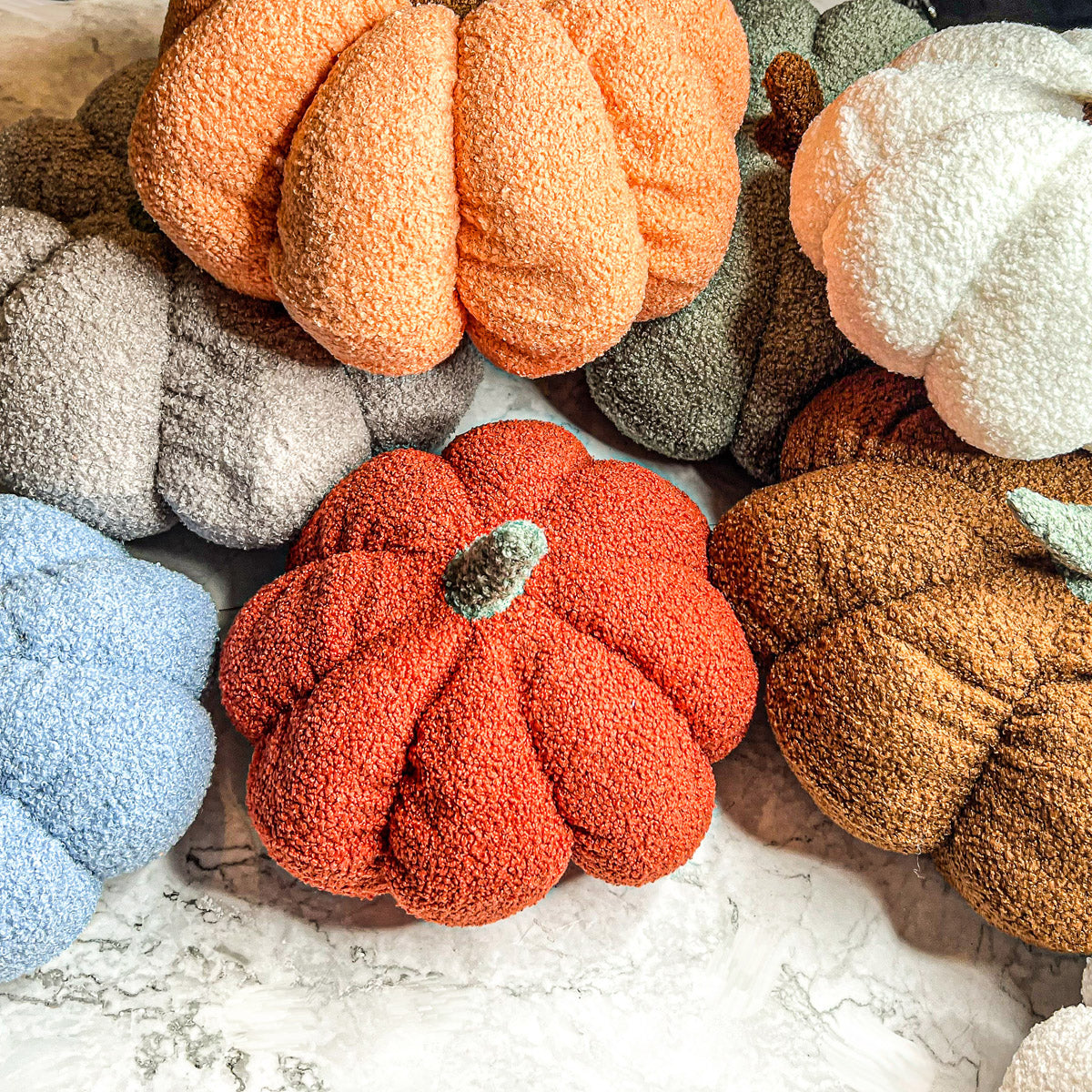 A collection of plush Blair Pumpkins in various colors including blue, gray, and orange, showcasing their soft texture and classic pumpkin shape.