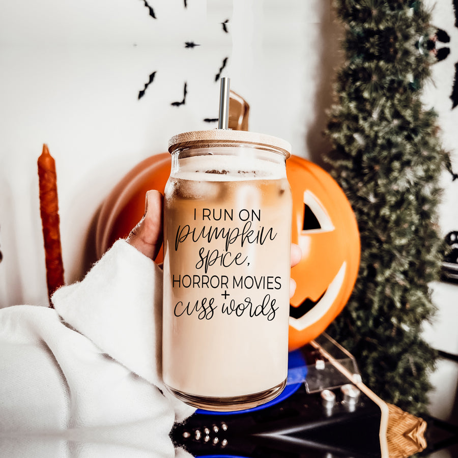 A stylish glass cup with a bamboo lid, featuring the phrase 'I RUN ON PUMPKIN SPICE, HORROR MOVIES + CUSS WORDS' in black graphic design.