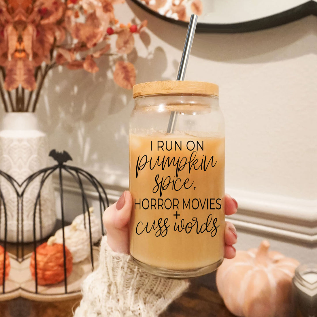 A stylish glass cup with a bamboo lid, featuring the phrase 'I RUN ON PUMPKIN SPICE, HORROR MOVIES + CUSS WORDS' in black graphic design.