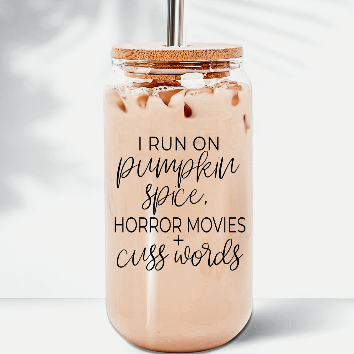 A stylish glass cup with a bamboo lid, featuring the phrase 'I RUN ON PUMPKIN SPICE, HORROR MOVIES + CUSS WORDS' in black graphic design.