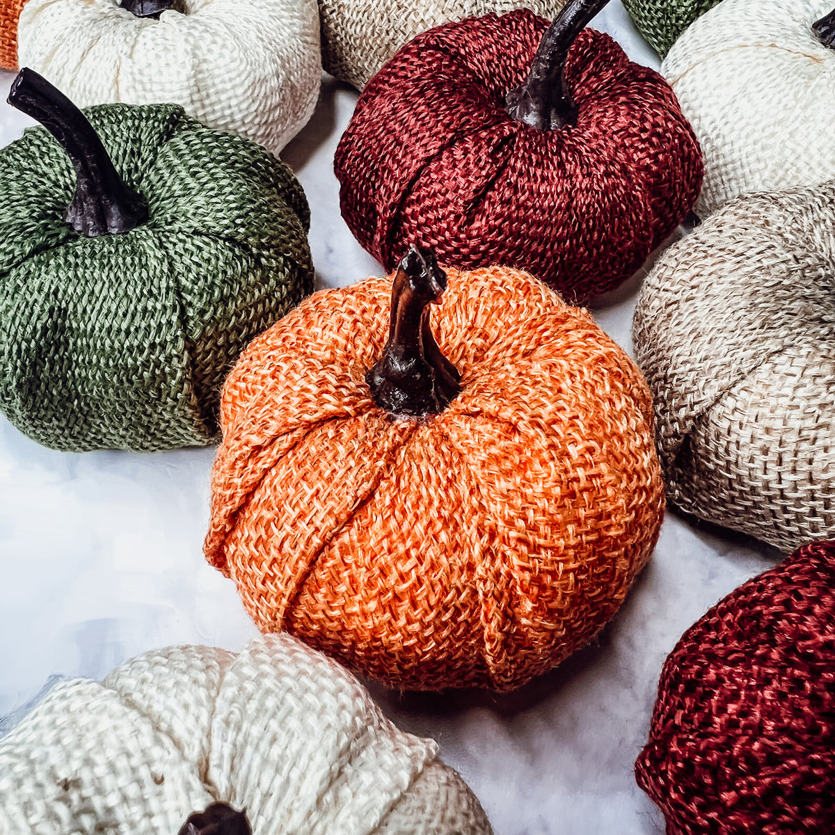 A collection of colorful jute mini pumpkins in various shades including burgundy, beige, green, ivory, and orange, perfect for fall decor.