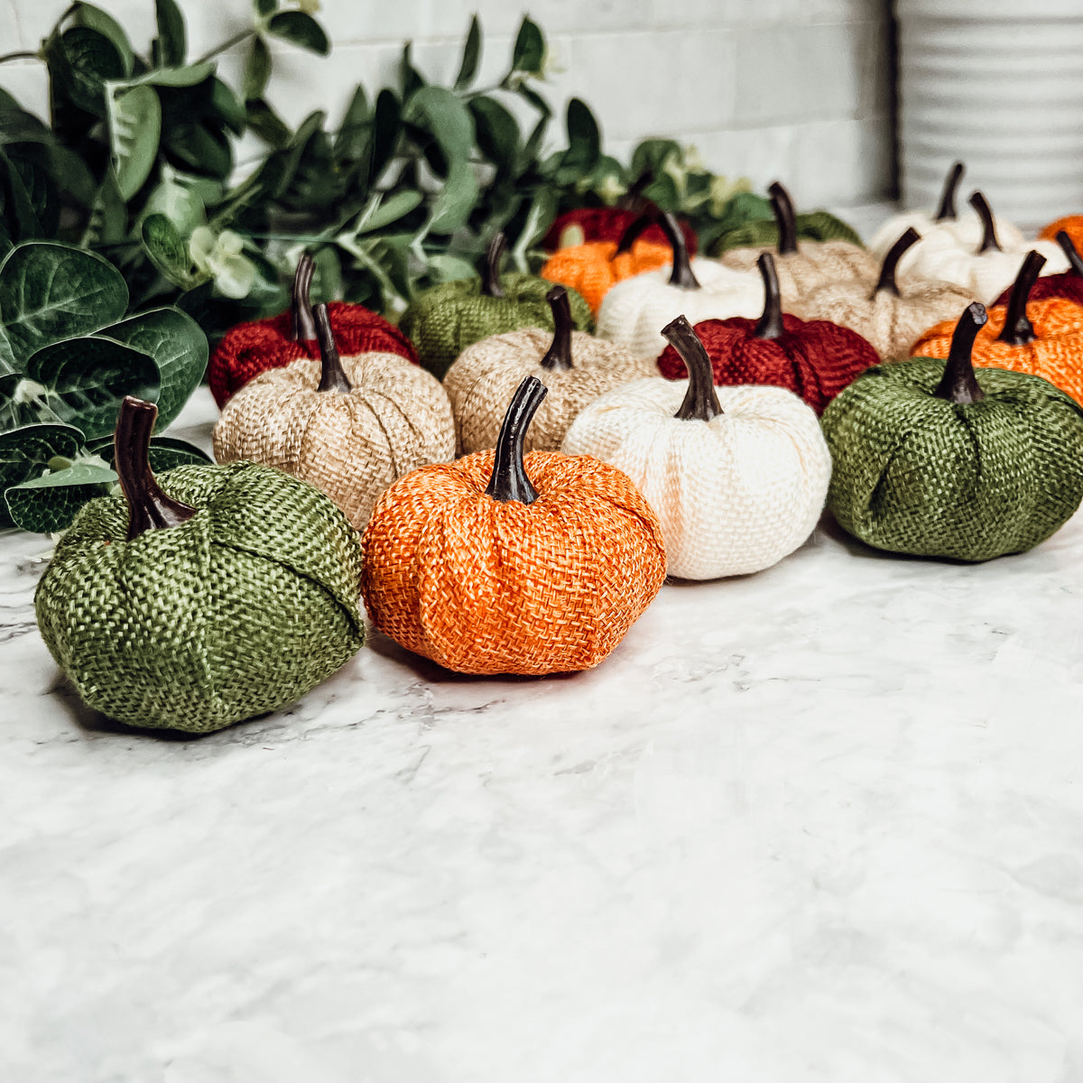 A collection of colorful jute mini pumpkins in various shades including burgundy, beige, green, ivory, and orange, perfect for fall decor.