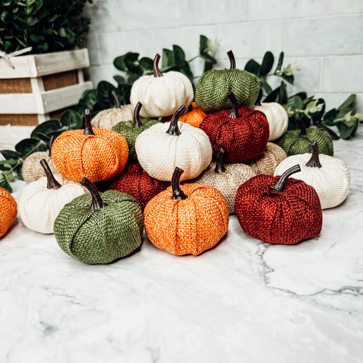 A collection of colorful jute mini pumpkins in various shades including burgundy, beige, green, ivory, and orange, perfect for fall decor.