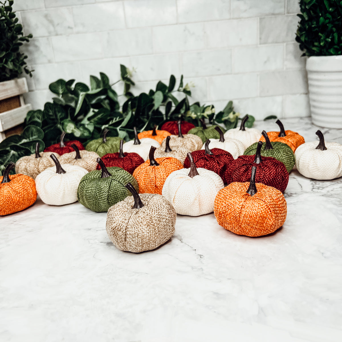 A collection of colorful jute mini pumpkins in various shades including burgundy, beige, green, ivory, and orange, perfect for fall decor.