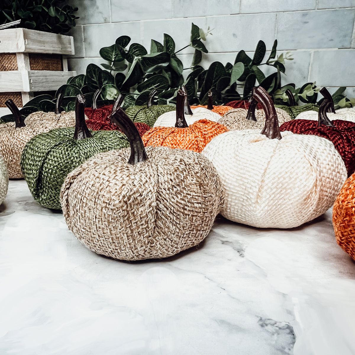 A collection of colorful jute mini pumpkins in various shades including burgundy, beige, green, ivory, and orange, perfect for fall decor.