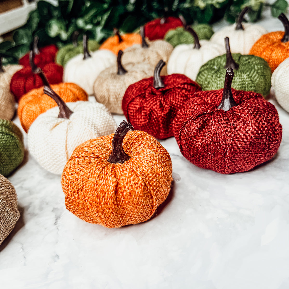 A collection of colorful jute mini pumpkins in various shades including burgundy, beige, green, ivory, and orange, perfect for fall decor.