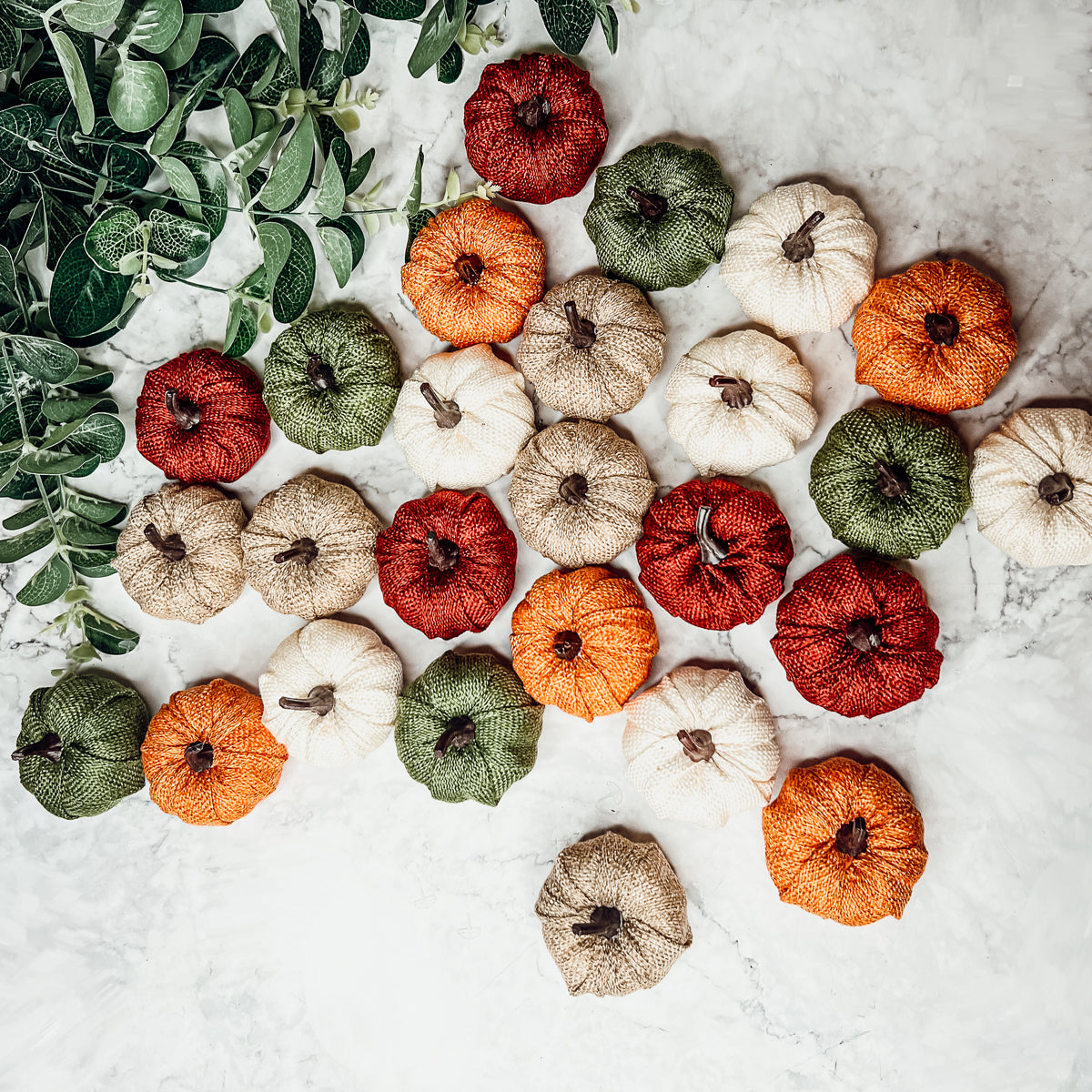 A collection of colorful jute mini pumpkins in various shades including burgundy, beige, green, ivory, and orange, perfect for fall decor.