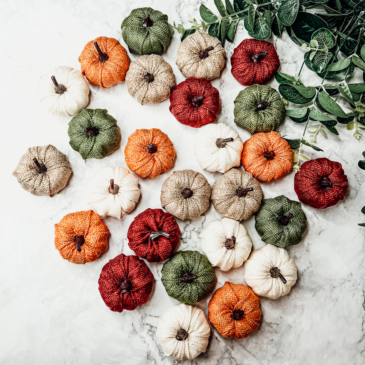 A collection of colorful jute mini pumpkins in various shades including burgundy, beige, green, ivory, and orange, perfect for fall decor.