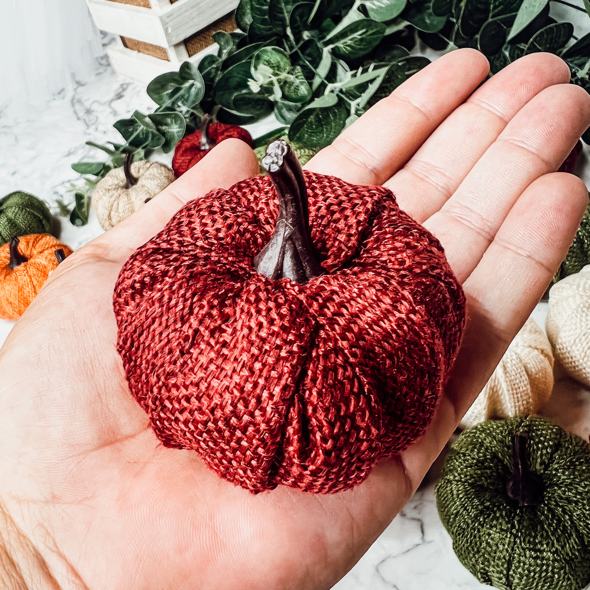 A collection of colorful jute mini pumpkins in various shades including burgundy, beige, green, ivory, and orange, perfect for fall decor.