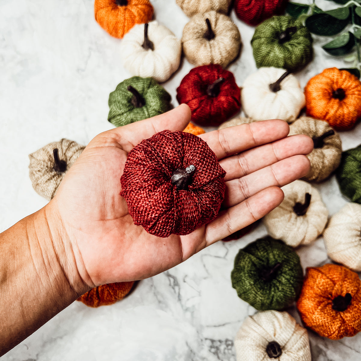 A collection of colorful jute mini pumpkins in various shades including burgundy, beige, green, ivory, and orange, perfect for fall decor.