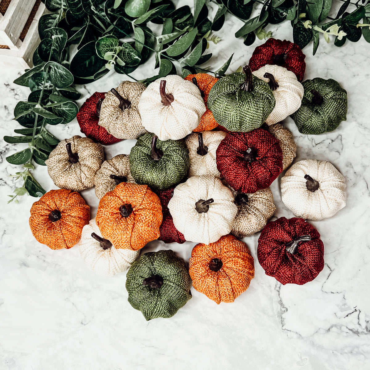 A collection of colorful jute mini pumpkins in various shades including burgundy, beige, green, ivory, and orange, perfect for fall decor.