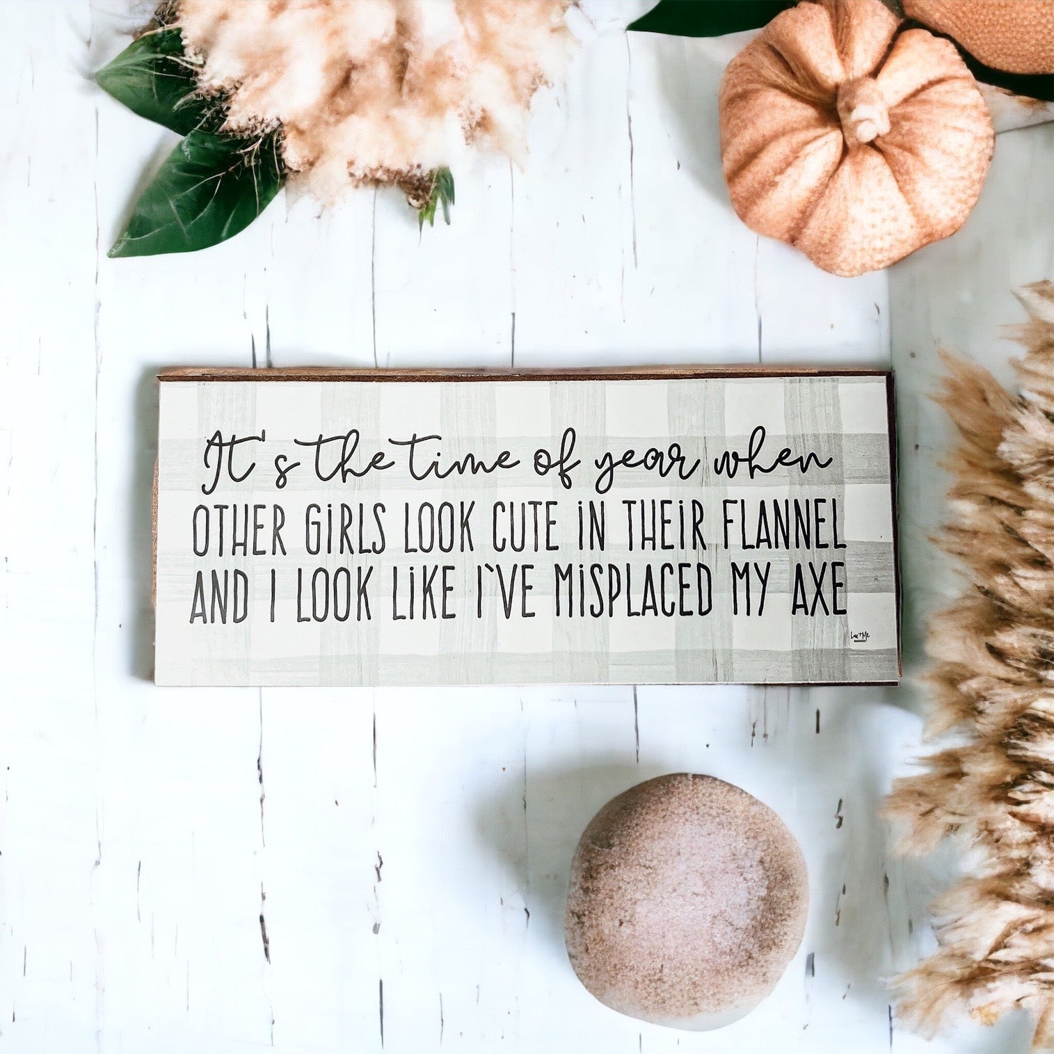 A humorous wooden sign with a flannel design reading 'It's the time of year when other girls look cute in their flannel and I look like I've misplaced my axe.'