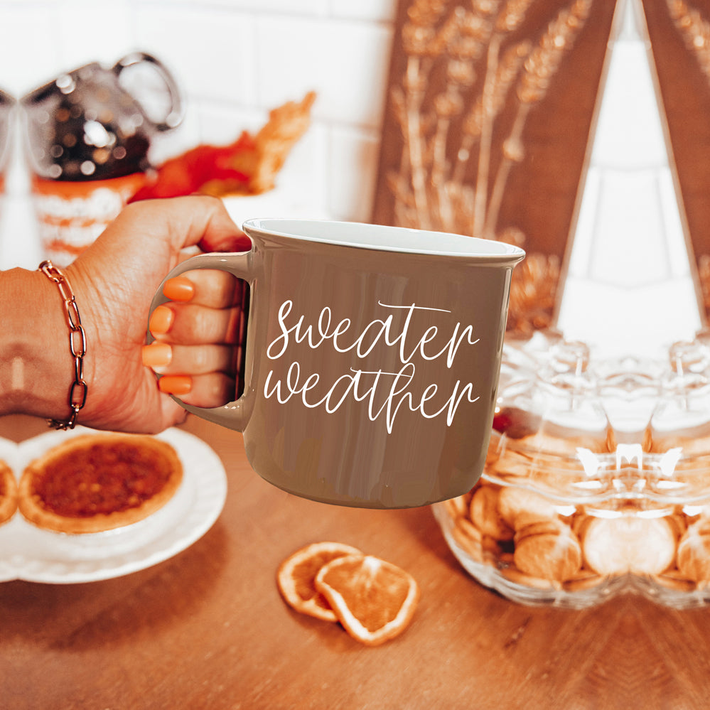 A cozy ceramic campfire style mug in neutral brown with white lettering that says 'Sweater Weather' on both sides.