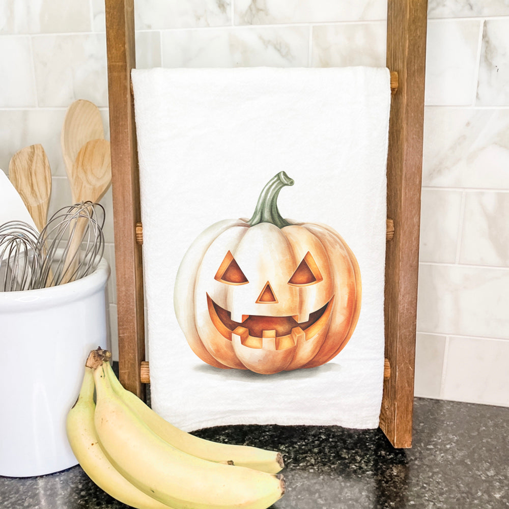 A vibrant watercolor carved pumpkin design on a 100% cotton tea towel, showcasing its absorbent texture and hemmed edges.