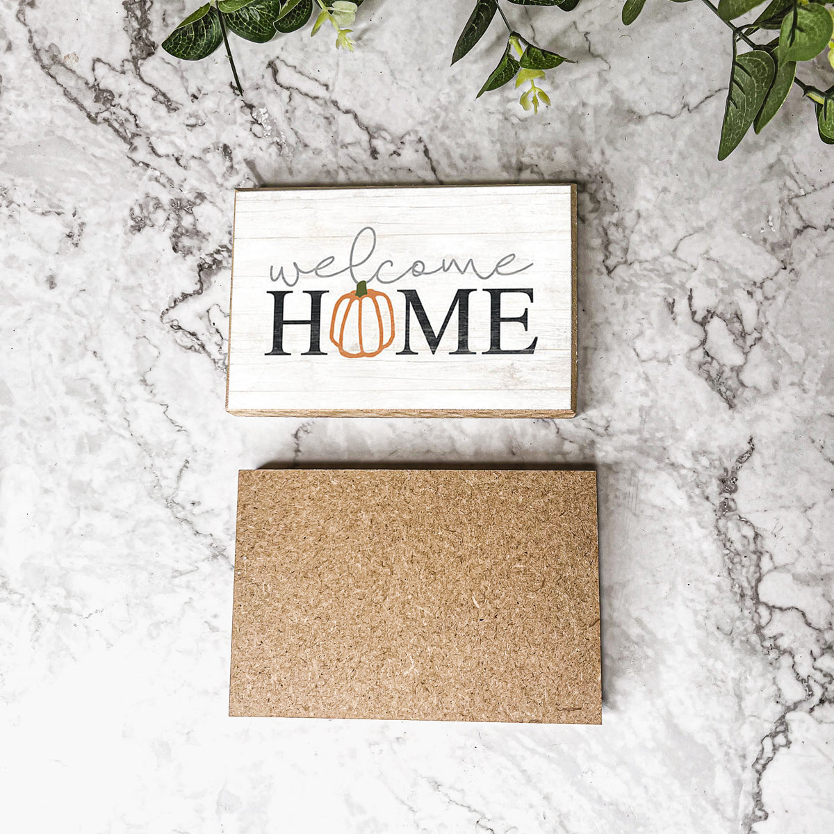 A handmade wooden sign reading 'Welcome Home' with a pumpkin graphic as the 'O', perfect for fall and Halloween decor.