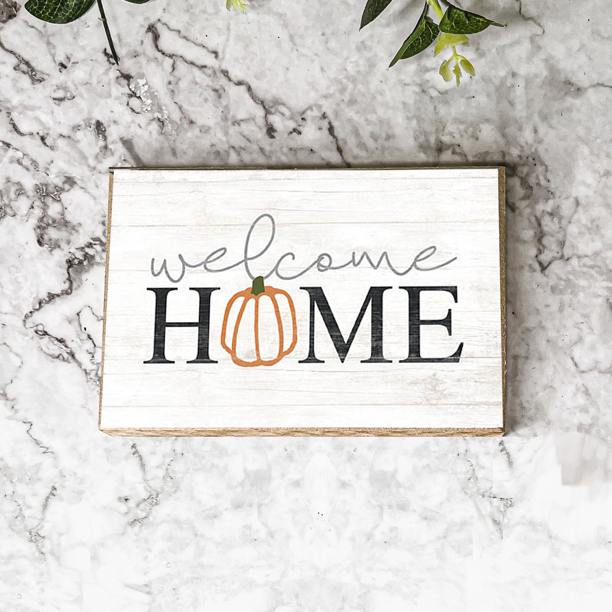 A handmade wooden sign reading 'Welcome Home' with a pumpkin graphic as the 'O', perfect for fall and Halloween decor.