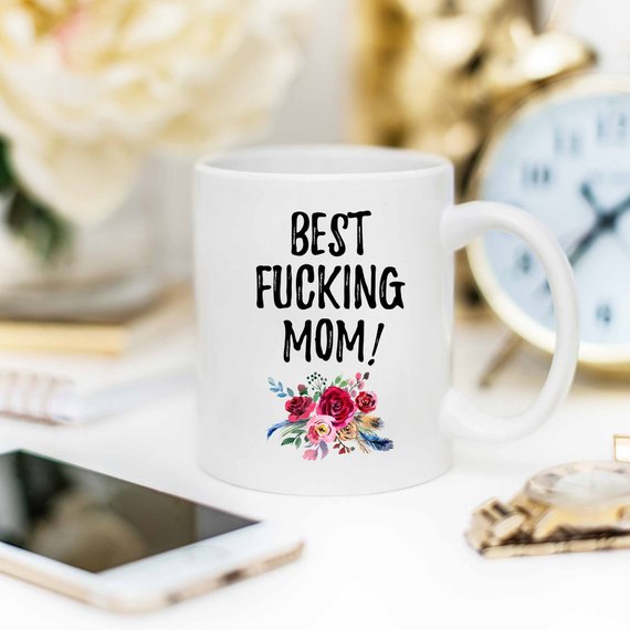 A white ceramic mug with 'Best Fucking Mom' printed in vibrant colors on both sides, showcasing a humorous and heartfelt design.