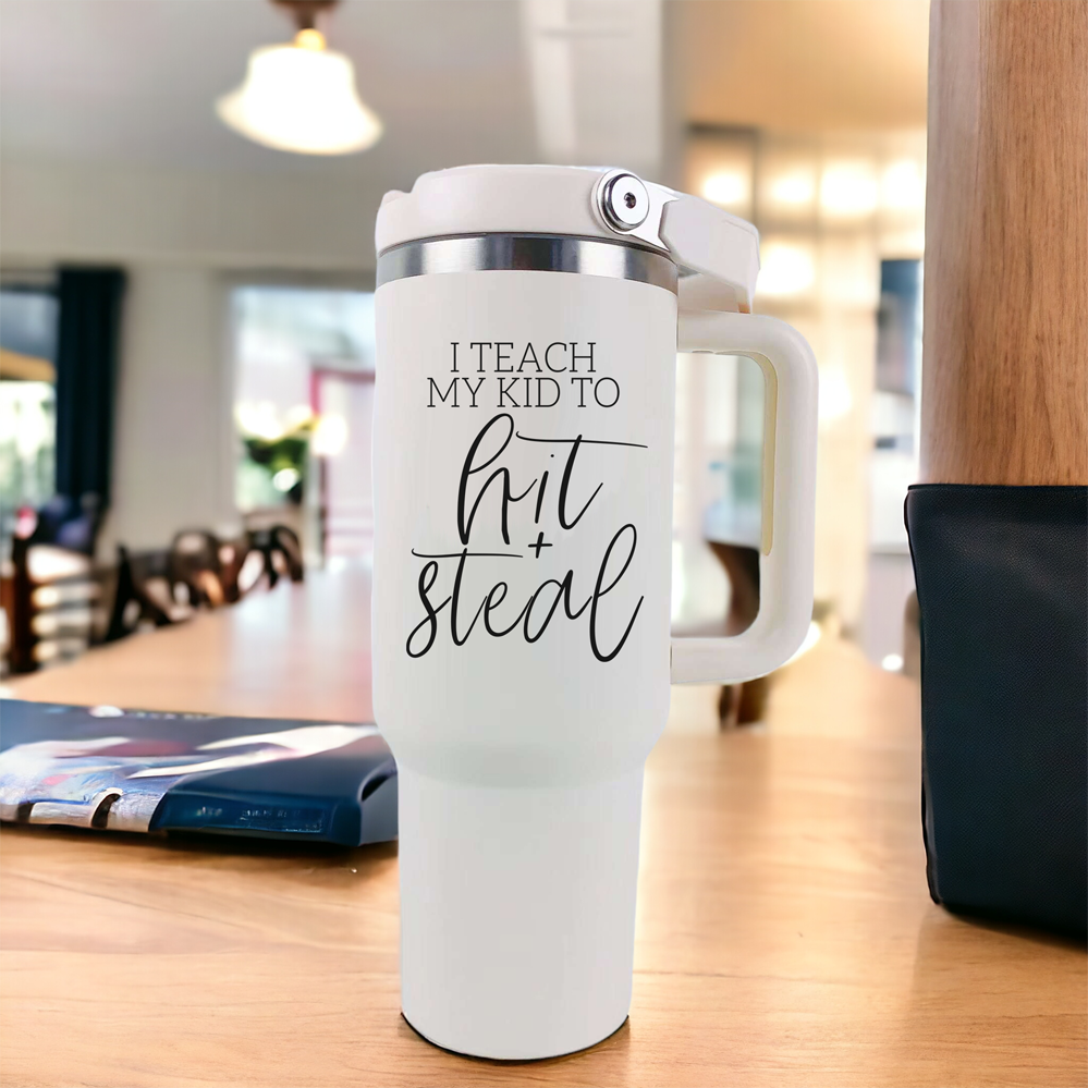 Hit & Steal tumbler with cream exterior and stainless steel interior, featuring a humorous design for baseball moms, double handles, and a no-spill sipping spout.