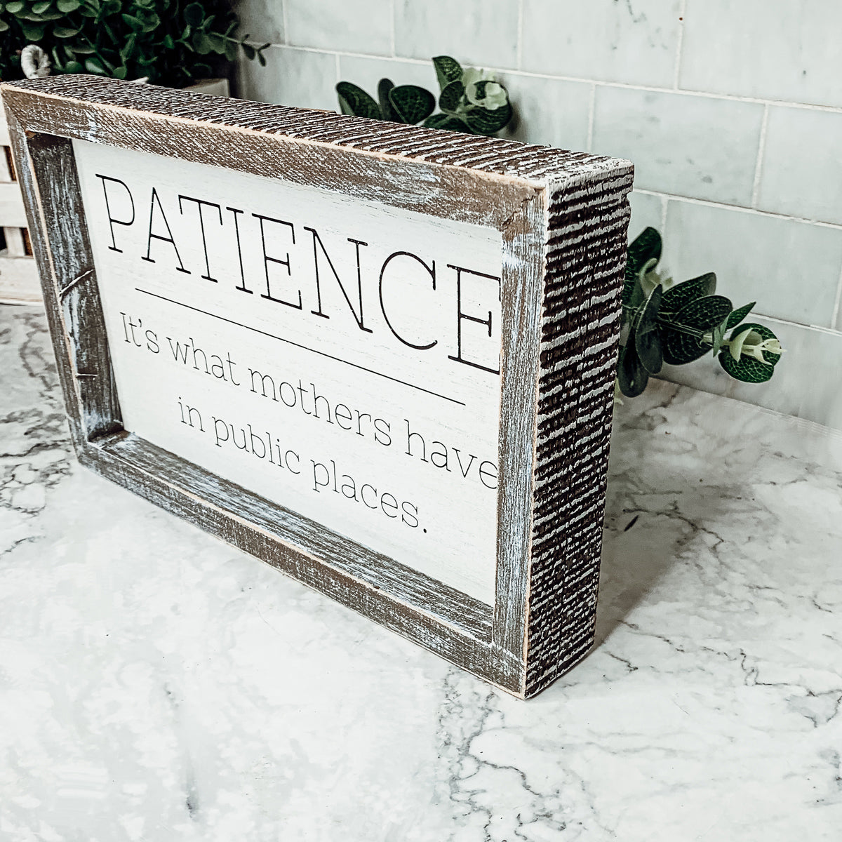 Wooden framed sign with the phrase 'Patience, It's What Mothers Have In Public Places', measuring 10" x 6" x 1.5", suitable for hanging or freestanding display.