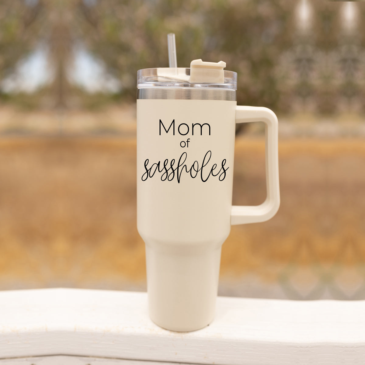 Mom of Sassholes 40oz insulated mug with handle, lid, and straw, featuring a cream exterior and black graphic design.