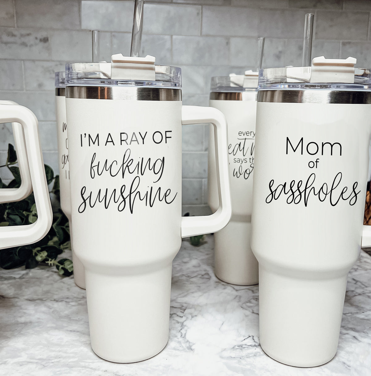 Mom of Sassholes 40oz insulated mug with handle, lid, and straw, featuring a cream exterior and black graphic design.