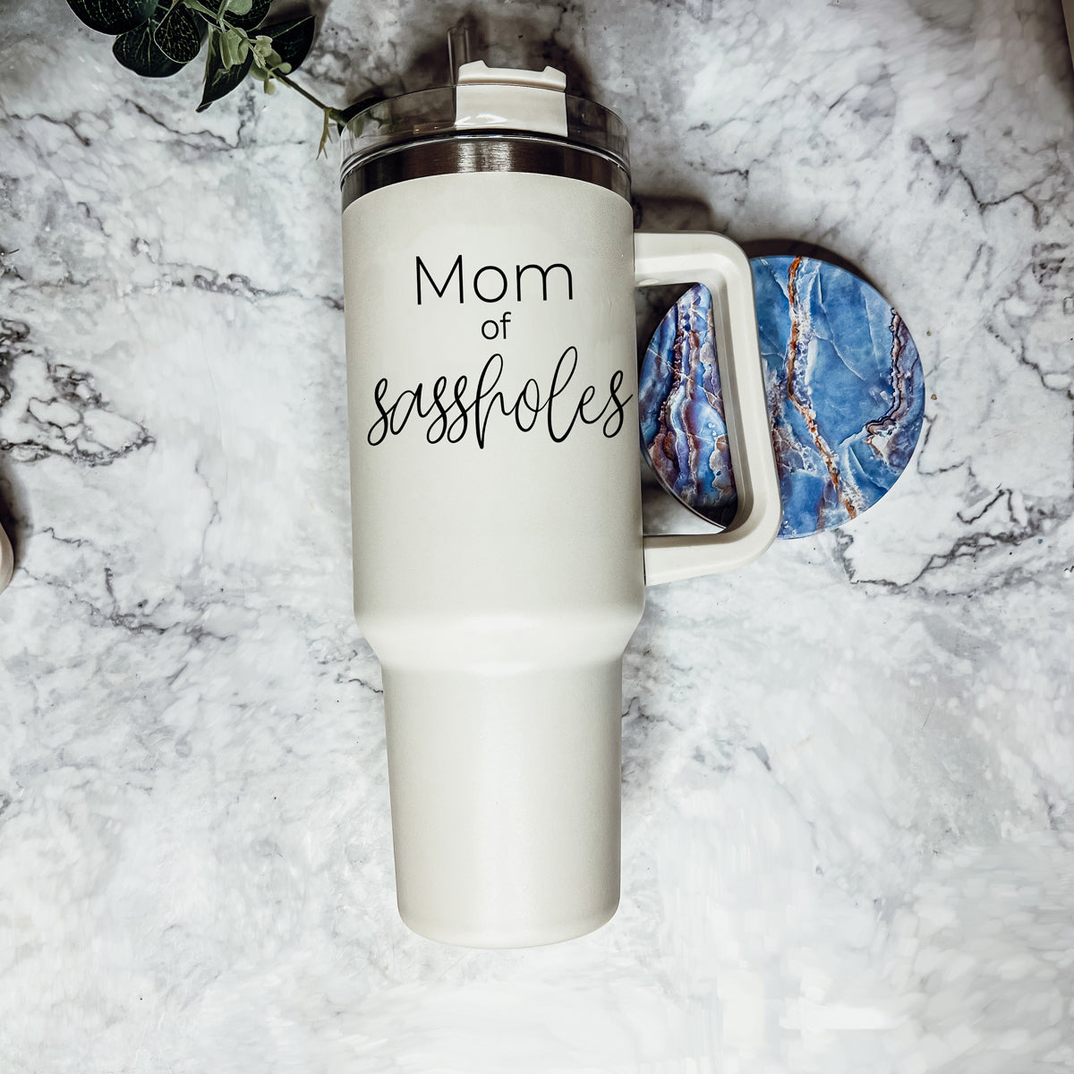 Mom of Sassholes 40oz insulated mug with handle, lid, and straw, featuring a cream exterior and black graphic design.