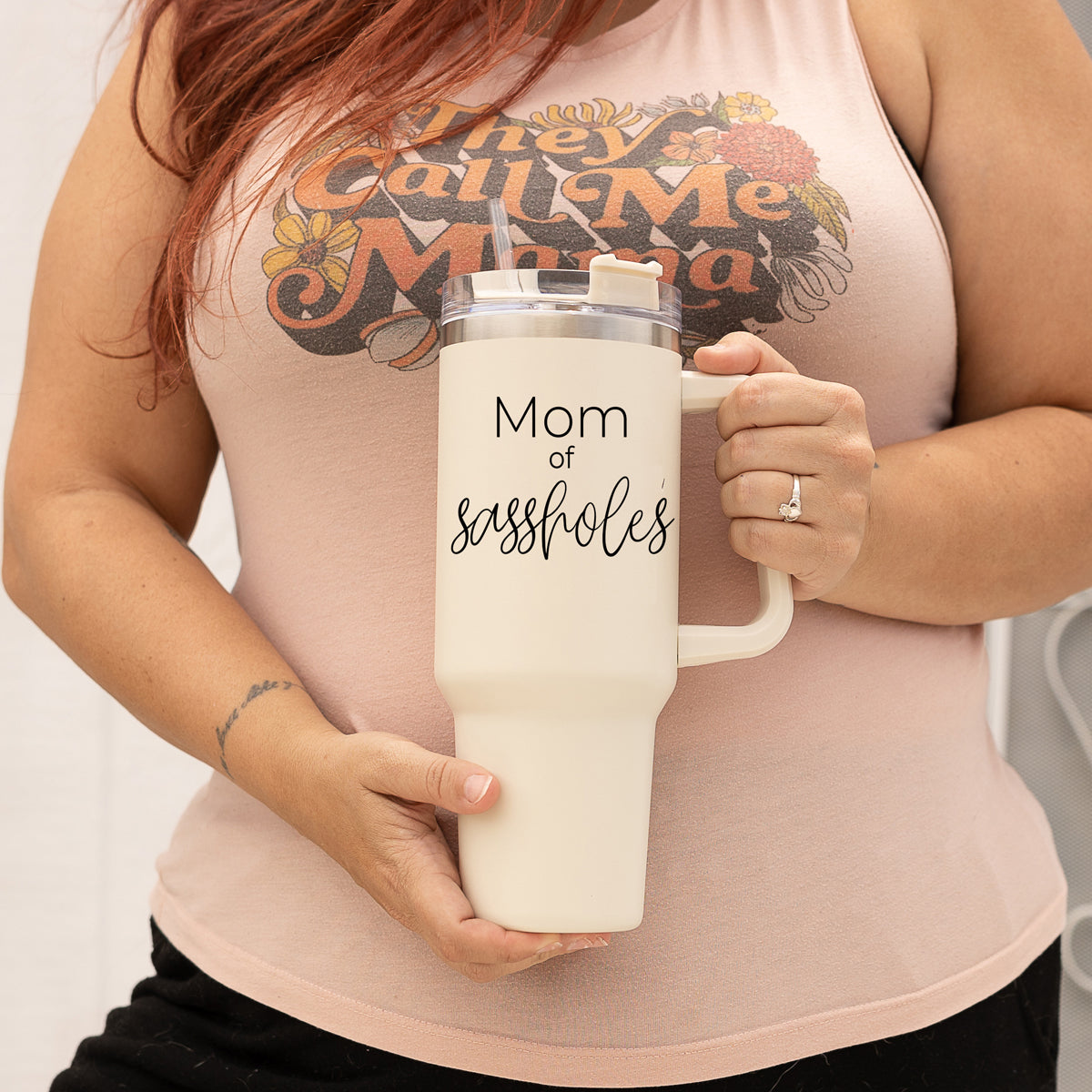 Mom of Sassholes 40oz insulated mug with handle, lid, and straw, featuring a cream exterior and black graphic design.