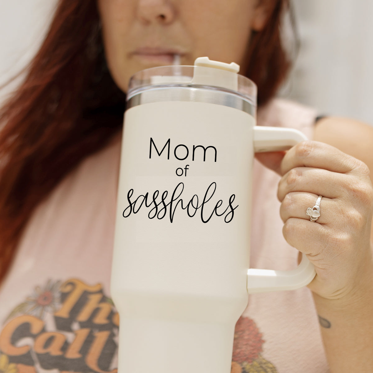 Mom of Sassholes 40oz insulated mug with handle, lid, and straw, featuring a cream exterior and black graphic design.