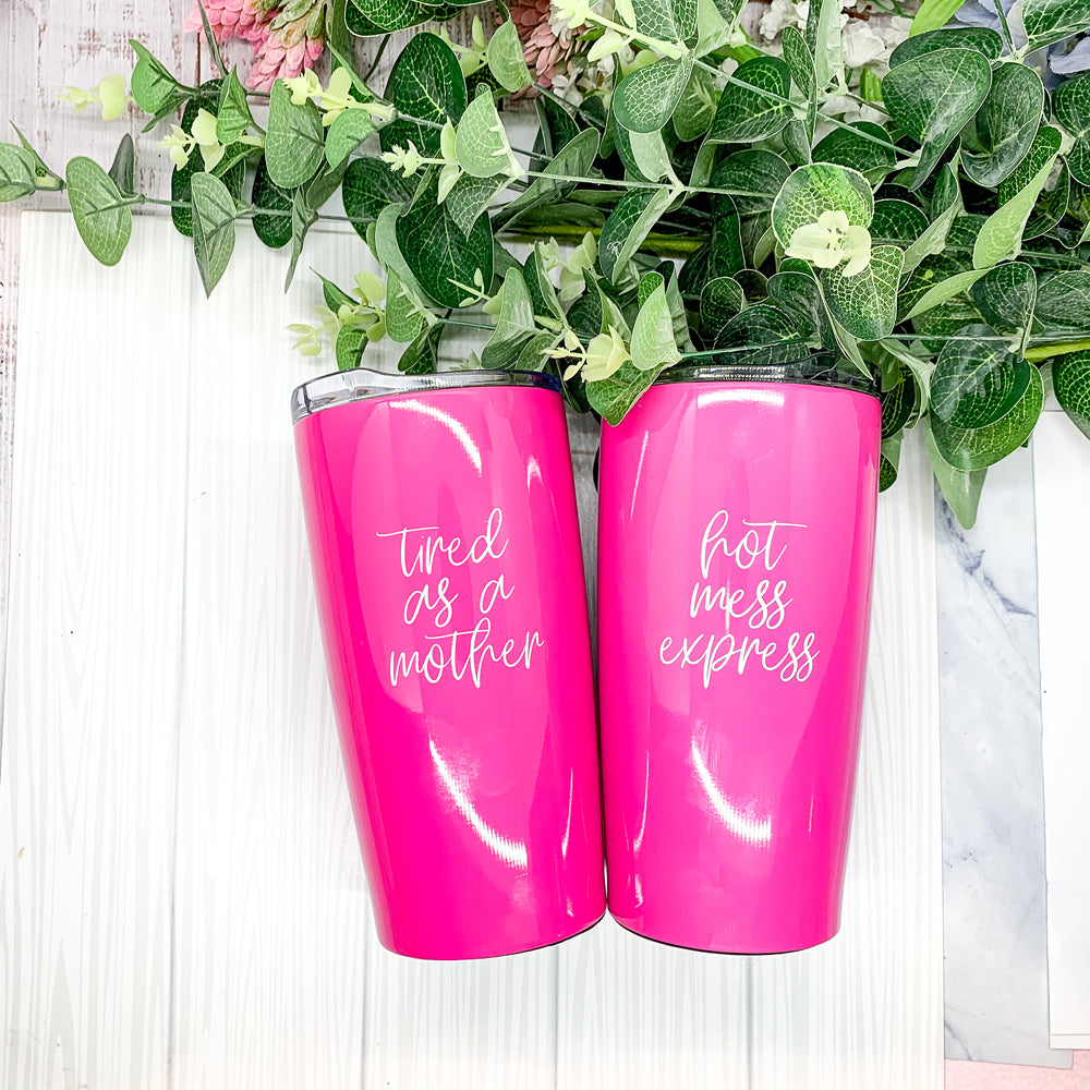 A stylish pink stainless steel travel mug with the phrase 'Tired as a Mother' printed on it, featuring a push-on lid and a non-skid foam bottom.