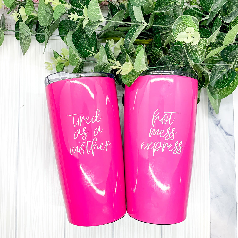 A stylish pink stainless steel travel mug with the phrase 'Tired as a Mother' printed on it, featuring a push-on lid and a non-skid foam bottom.