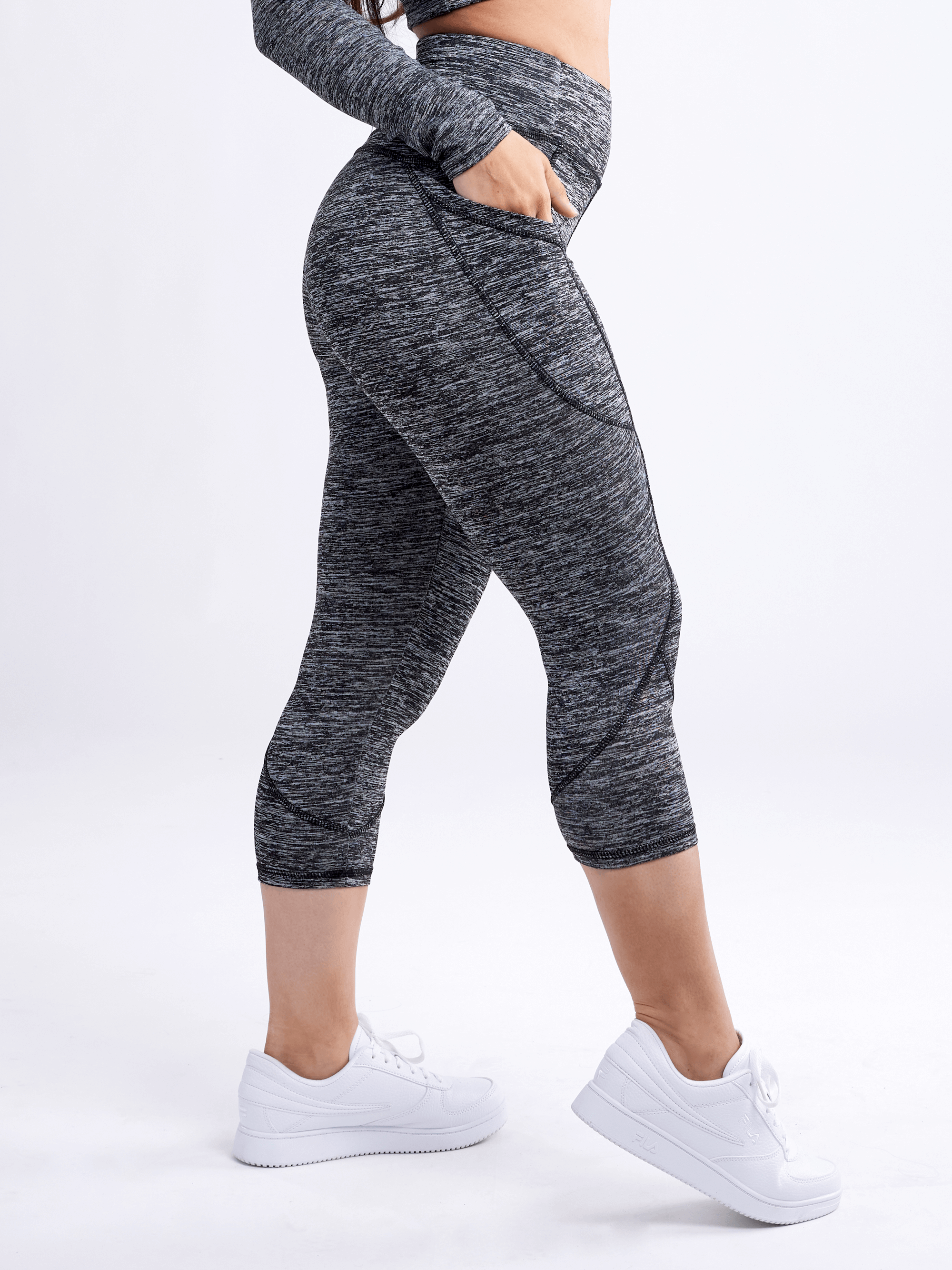 A pair of stylish mid-rise capri fitness leggings in black with side pockets, designed for women, showcasing a smooth and silky fabric.