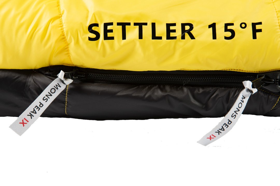 Settler 15 F sleeping bag displayed outdoors, showcasing its dual zippers, soft nylon fabric, and hood with cinch draw cords.