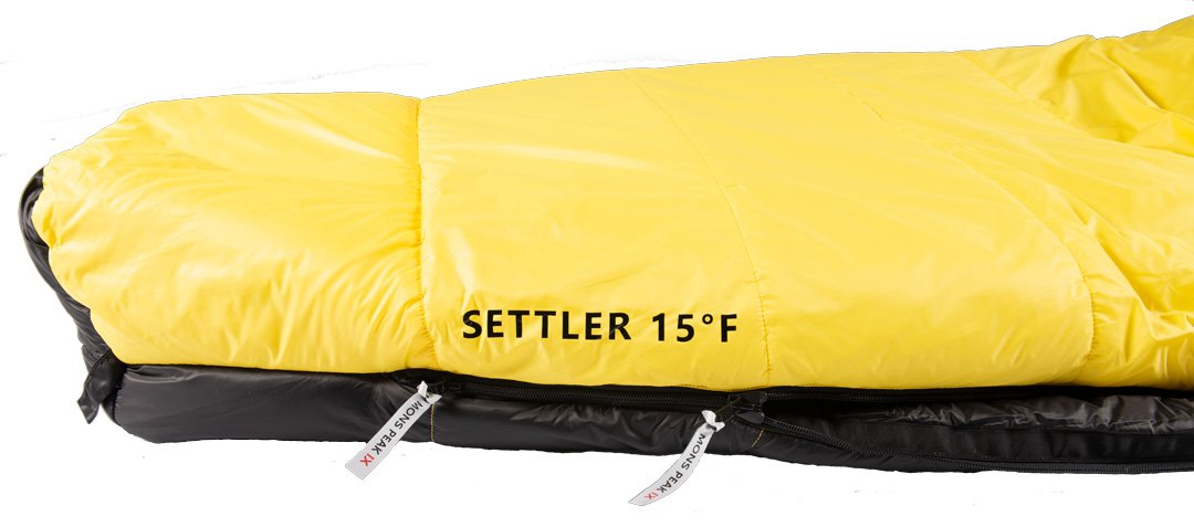 Settler 15 F sleeping bag displayed outdoors, showcasing its dual zippers, soft nylon fabric, and hood with cinch draw cords.