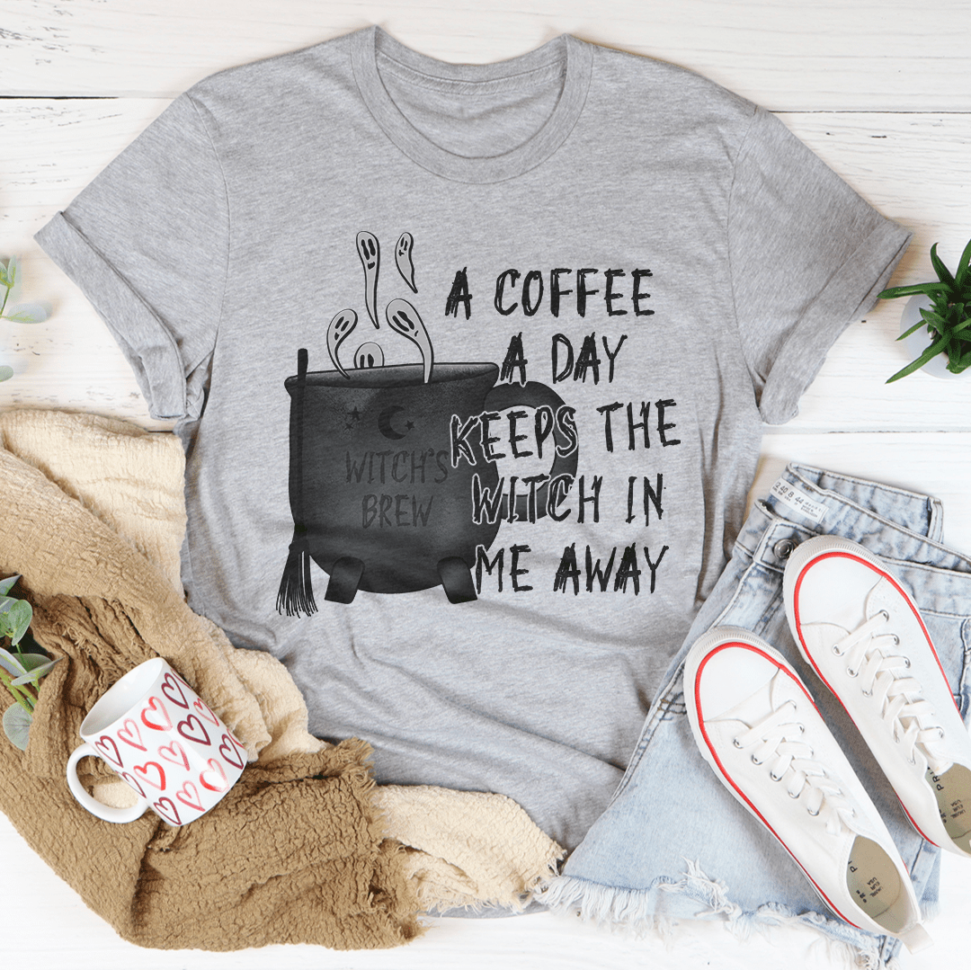 A stylish black t-shirt with the phrase 'A Coffee A Day Keeps The Witch In Me Away' printed in white, showcasing its soft fabric and durable stitching.