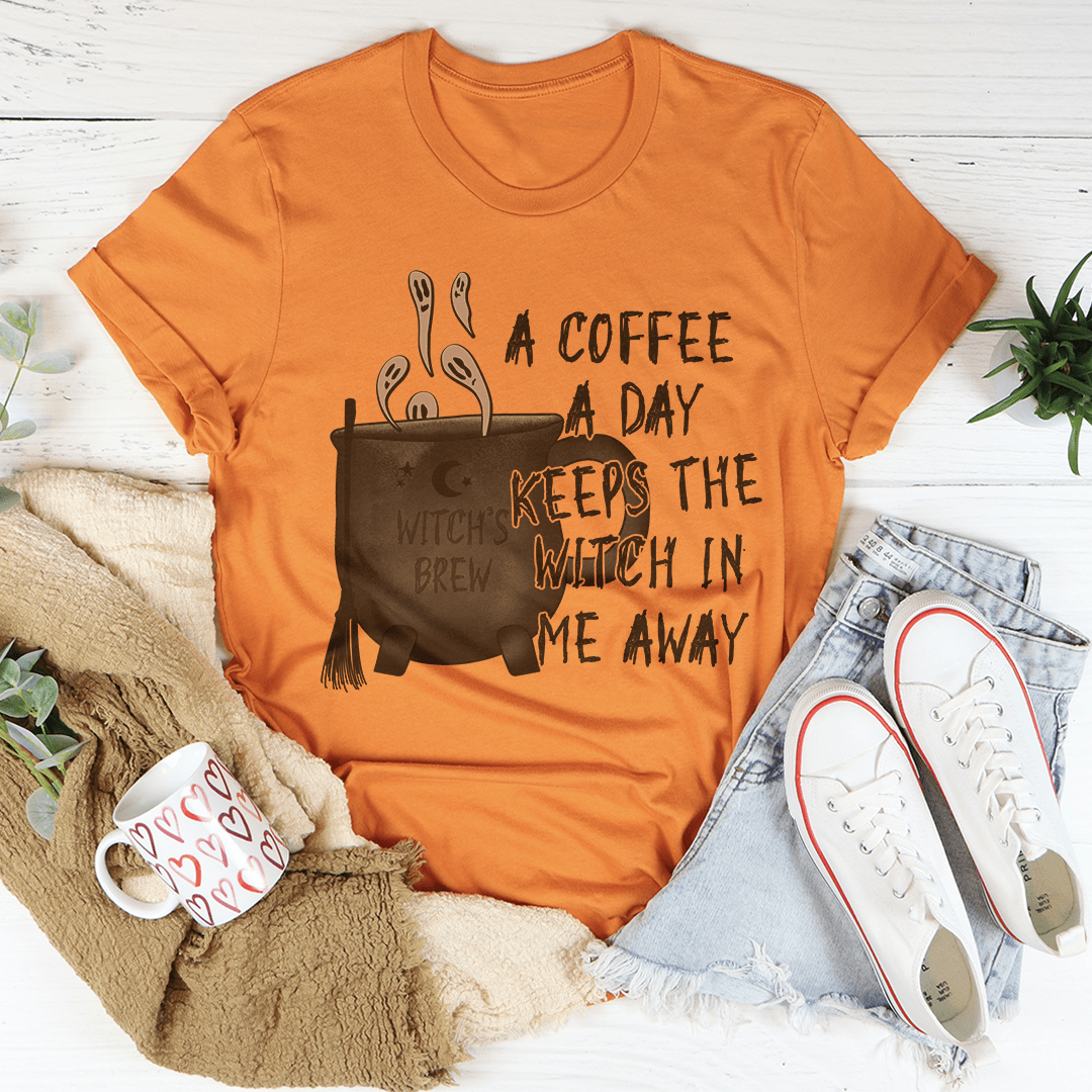 A stylish black t-shirt with the phrase 'A Coffee A Day Keeps The Witch In Me Away' printed in white, showcasing its soft fabric and durable stitching.